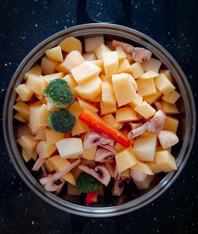 Diced potatoes carrots broccoli and mushrooms boiling together in a pot before roasting