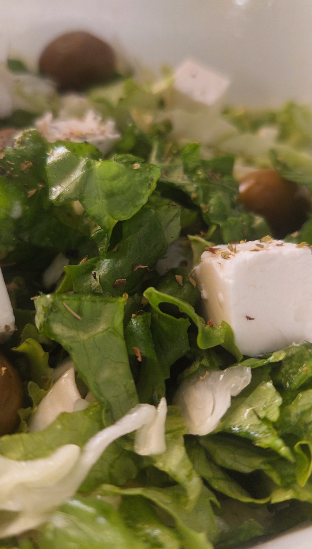 Mixed lettuce and cabbage salad in a bowl. Placed on a brown table, there is a keybord nex to it.