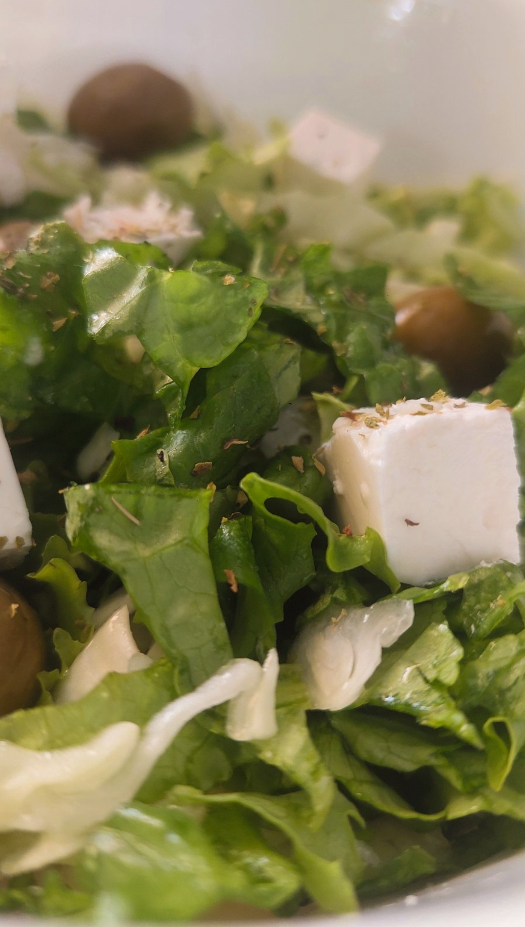 Mixed lettuce and cabbage salad in a bowl. Placed on a brown table, there is a keybord nex to it.