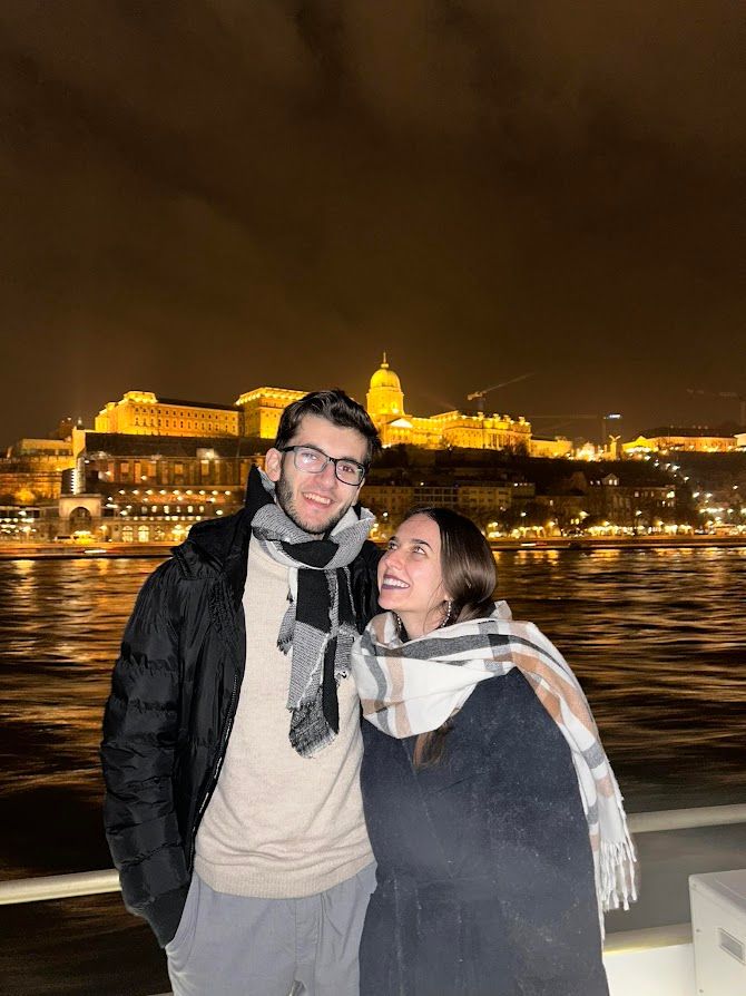 A couple raising a champagne toast on a Danube night cruise with famous buildings illuminated