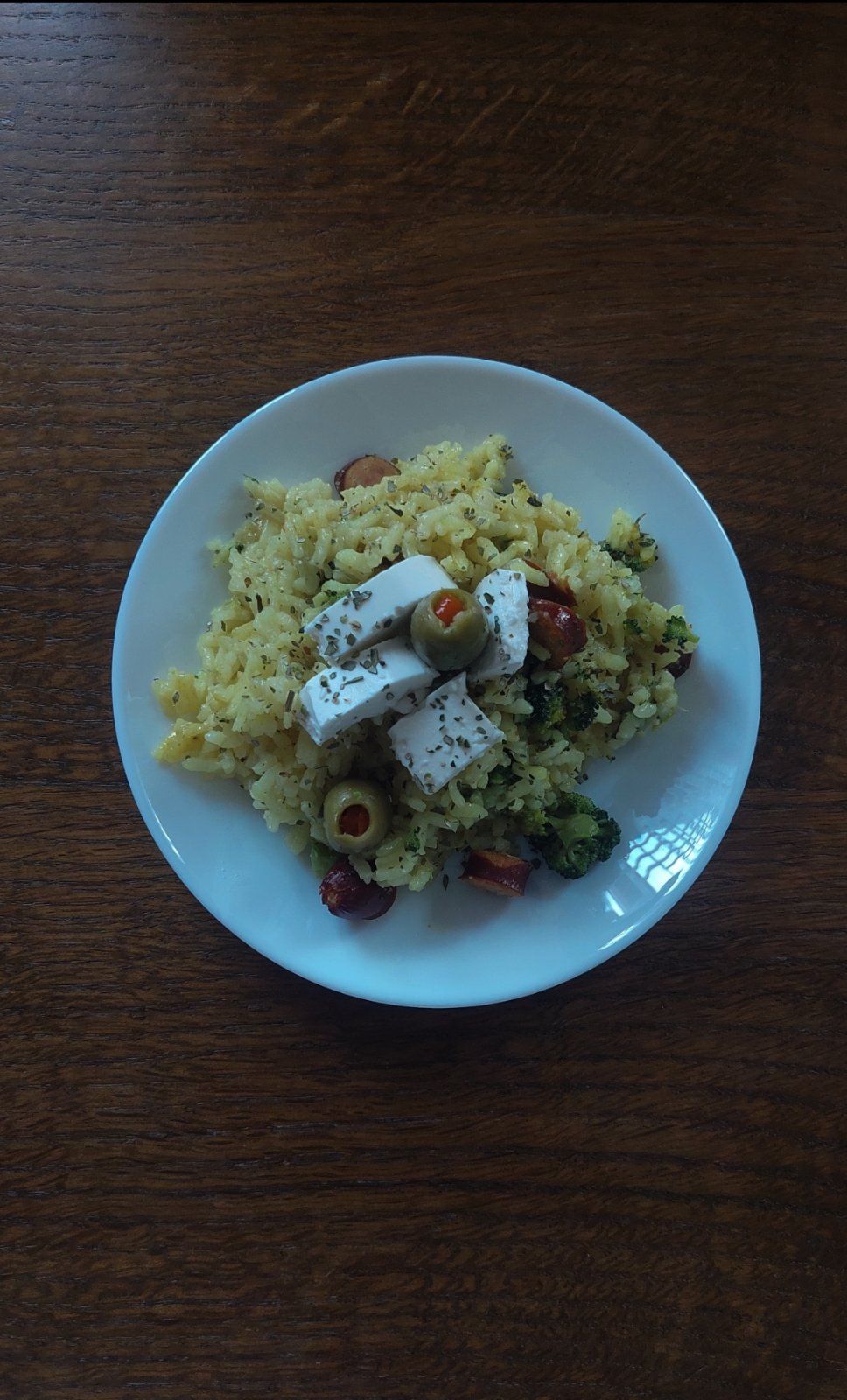 Rice with broccoli served on a plate decorated with cheese and olives sprinkled with oregano