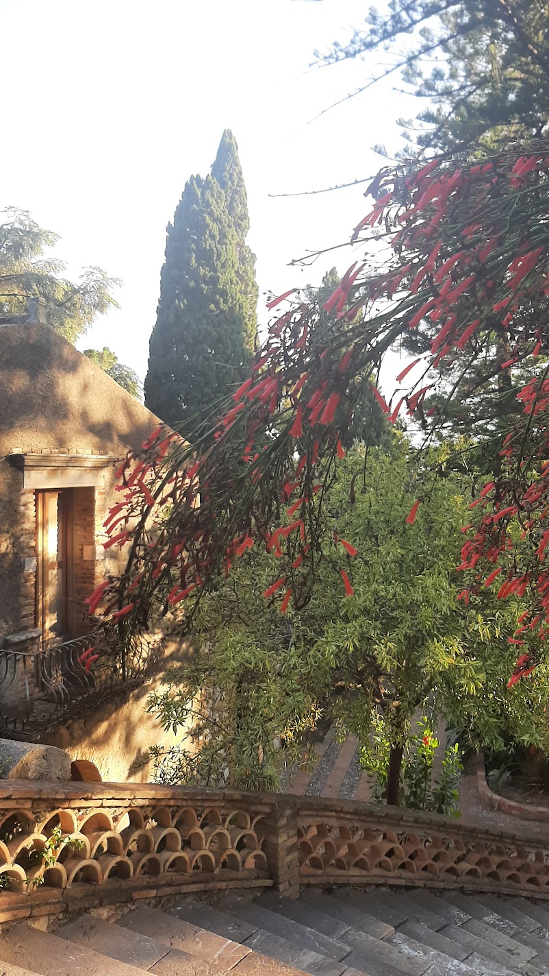 Red cuphea flowers and a stone building in the terraced gardens of Villa Comunale in Taormina