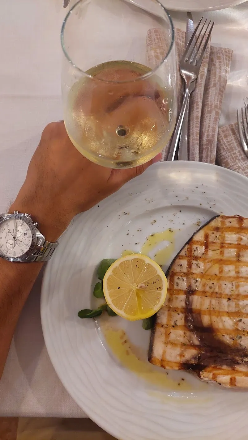 Grilled swordfish with lemon and a glass of white wine on a restaurant table in Taormina
