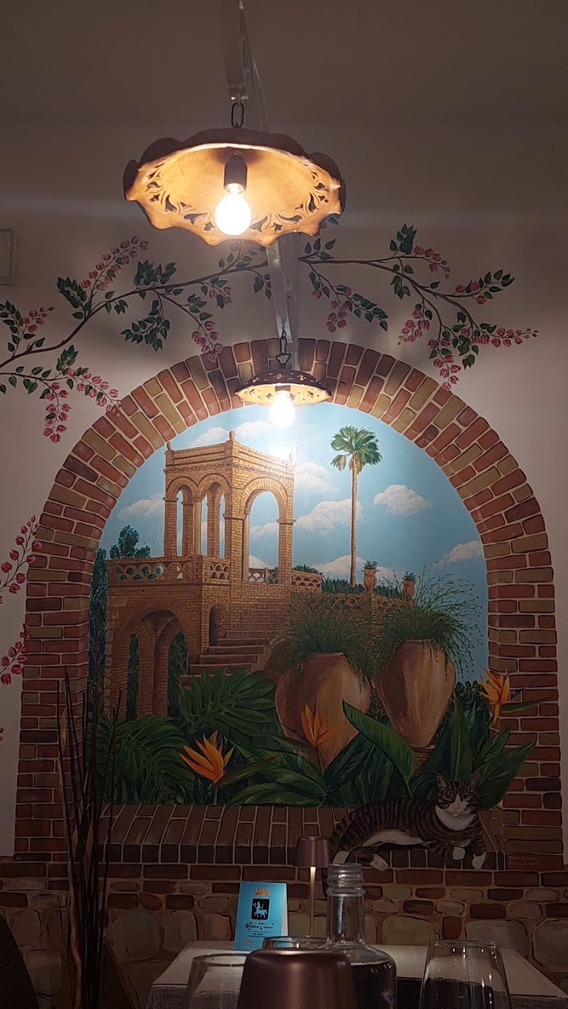 A painted trompe-l'oeil garden mural with a cat on a ledge in a Castelmola restaurant
