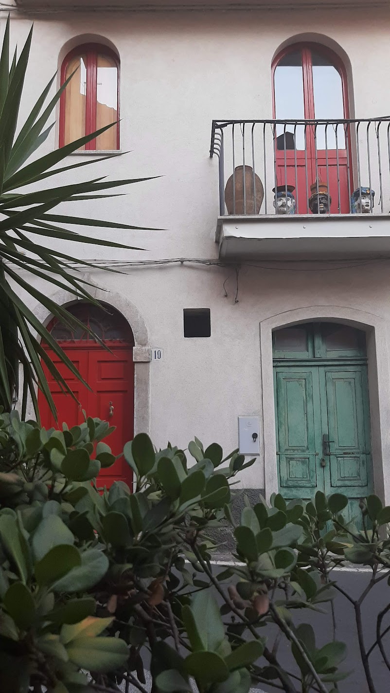 A Sicilian house facade with red and green arched doors and ceramic Moor's head planters on the balcony