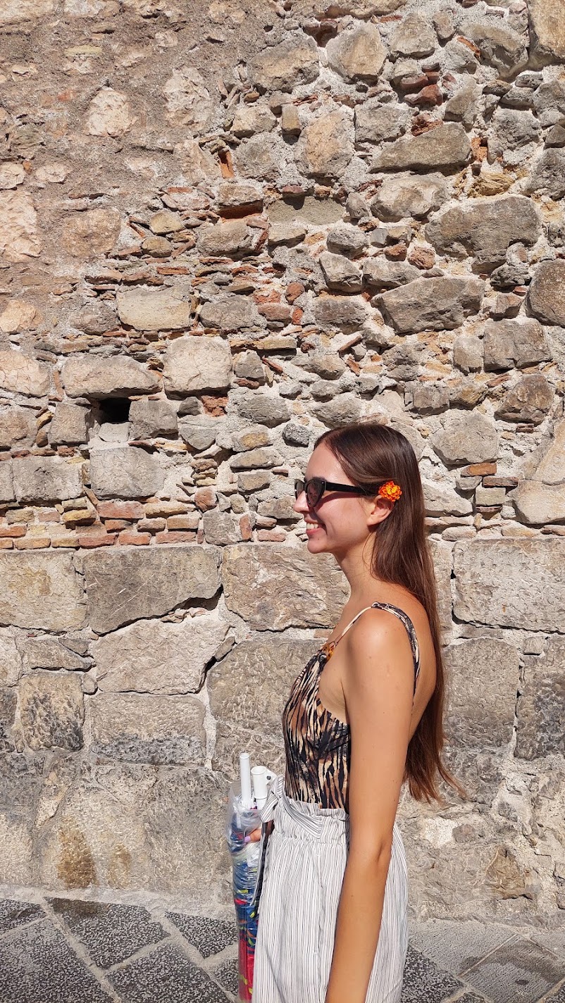 A woman smiling in profile beside an ancient stone wall in Taormina