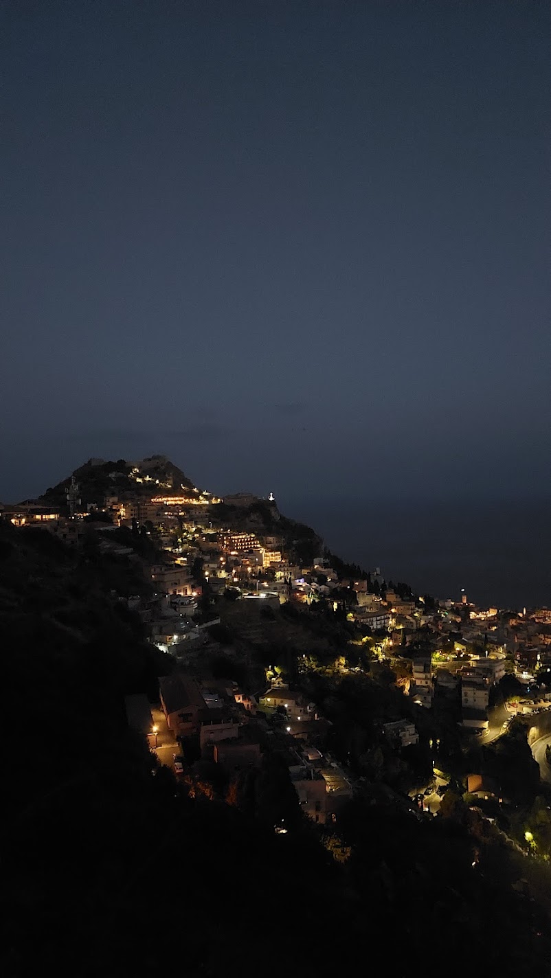 The lights of a hillside town glowing at nightfall near Taormina