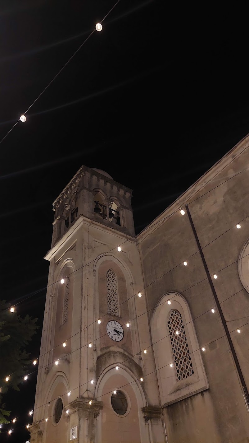 An illuminated church bell tower strung with festoon lights at night in Castelmola