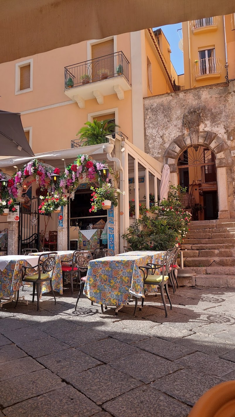 A Taormina restaurant terrace with a flower-decorated entrance and majolica-tiled tables