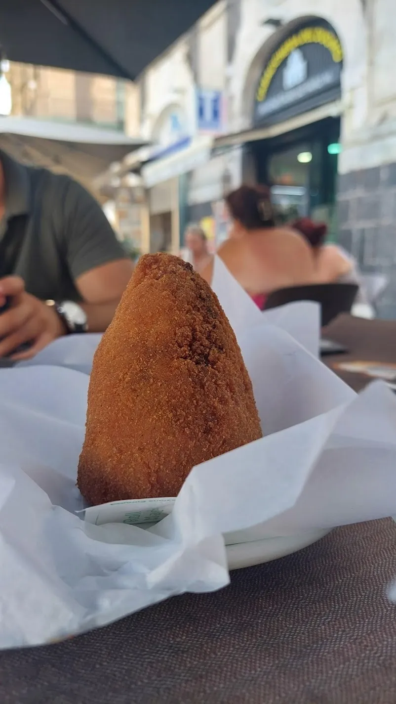 A golden fried arancino resting in paper at an outdoor café table in Sicily
