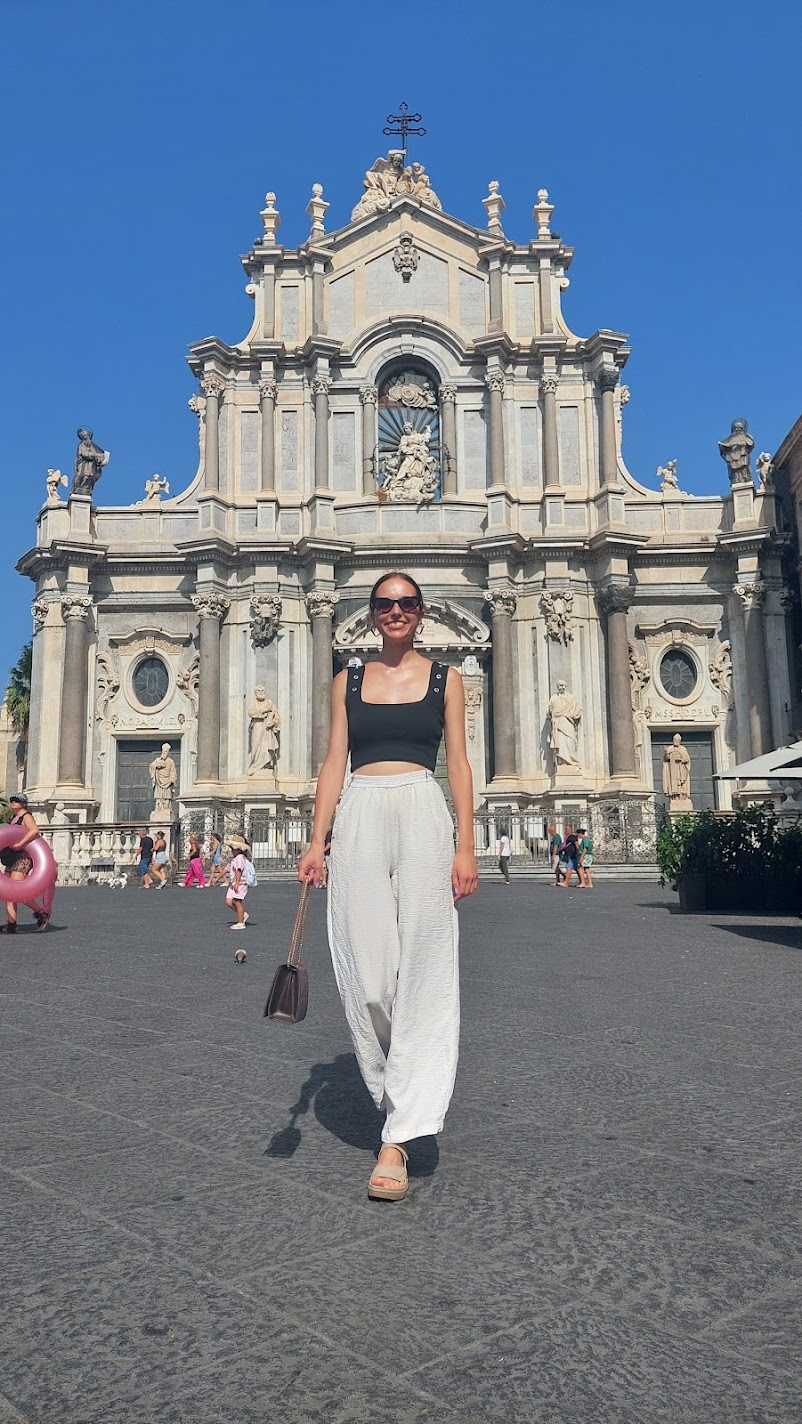 A woman standing in front of Saint Agatha's Cathedral on Piazza del Duomo in Catania under a blue sky