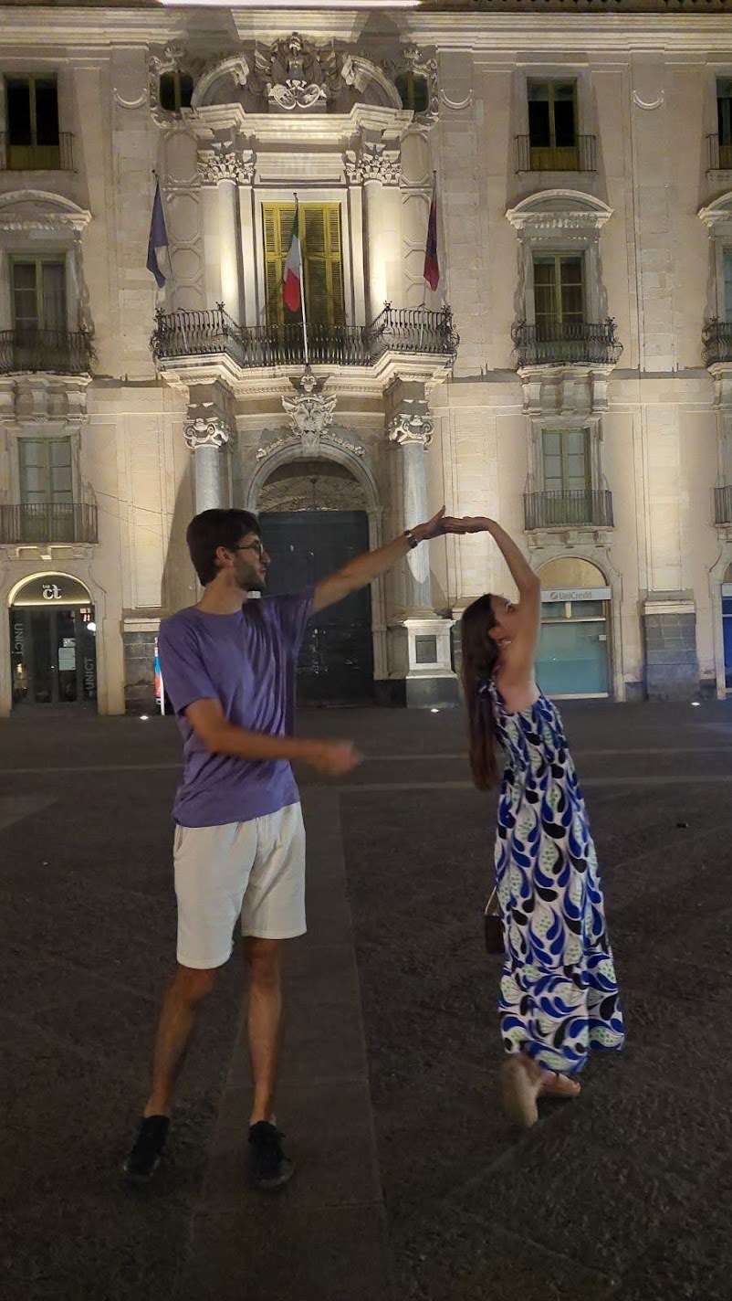 A couple dancing at night in a Catania square in front of a floodlit Baroque palazzo