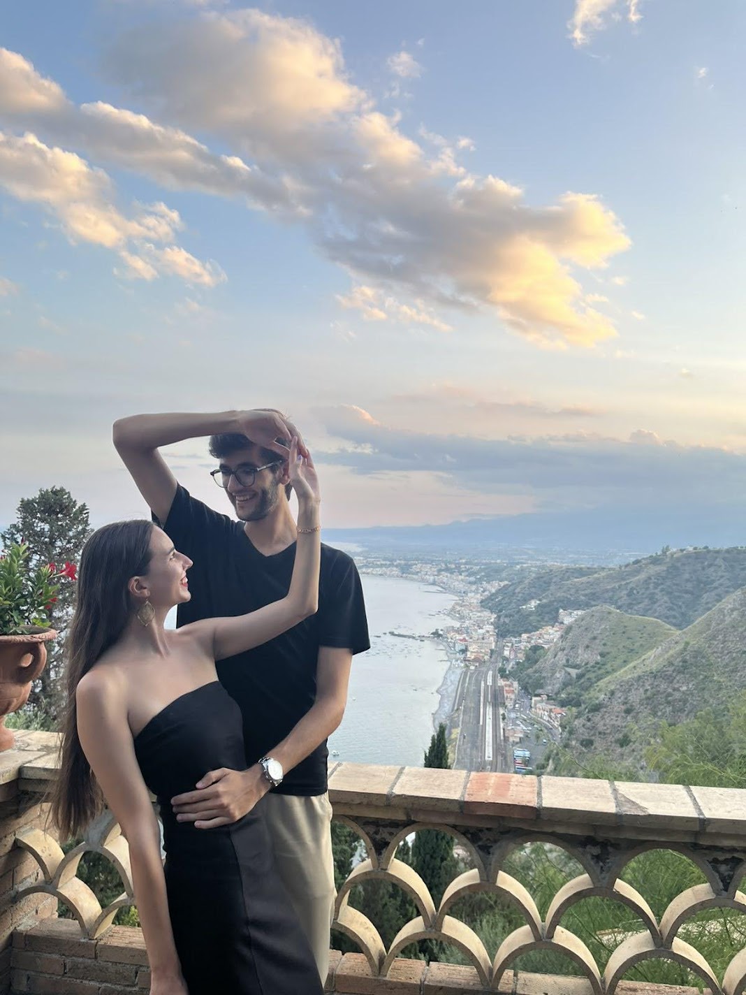 A couple embracing on the Villa Comunale terrace overlooking the coast at dusk in Taormina