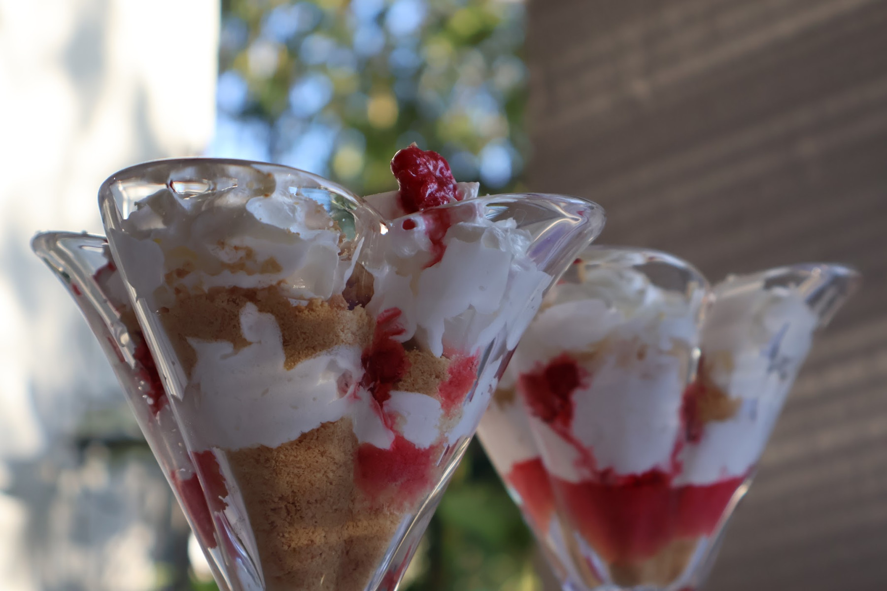 Two glasses of layered raspberry dessert with whipped cream and ground biscuits, topped with a fresh raspberry
