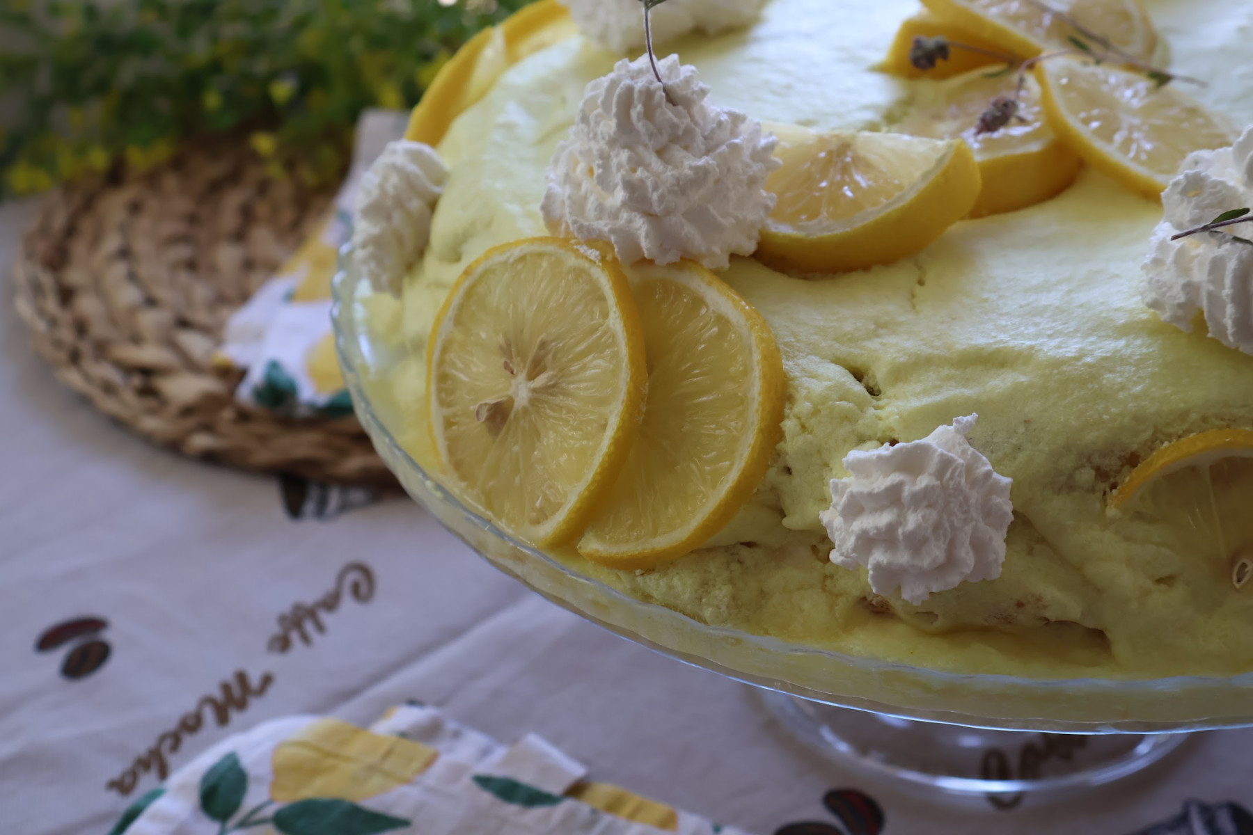 Side view of the lemon cake on a glass stand, with lemon slices and whipped cream rosettes around the edge