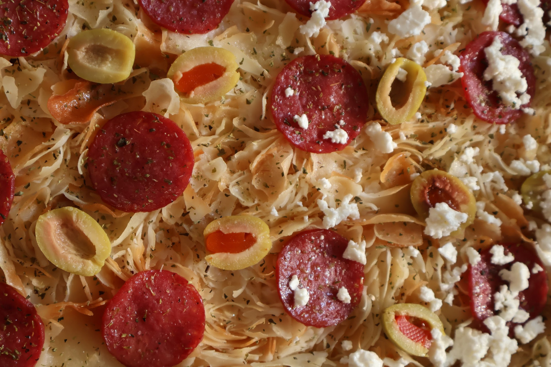 Close-up of the yufka tray bake topped with grated cheese, slices of kulen, stuffed green olives, crumbled white cheese and dried oregano