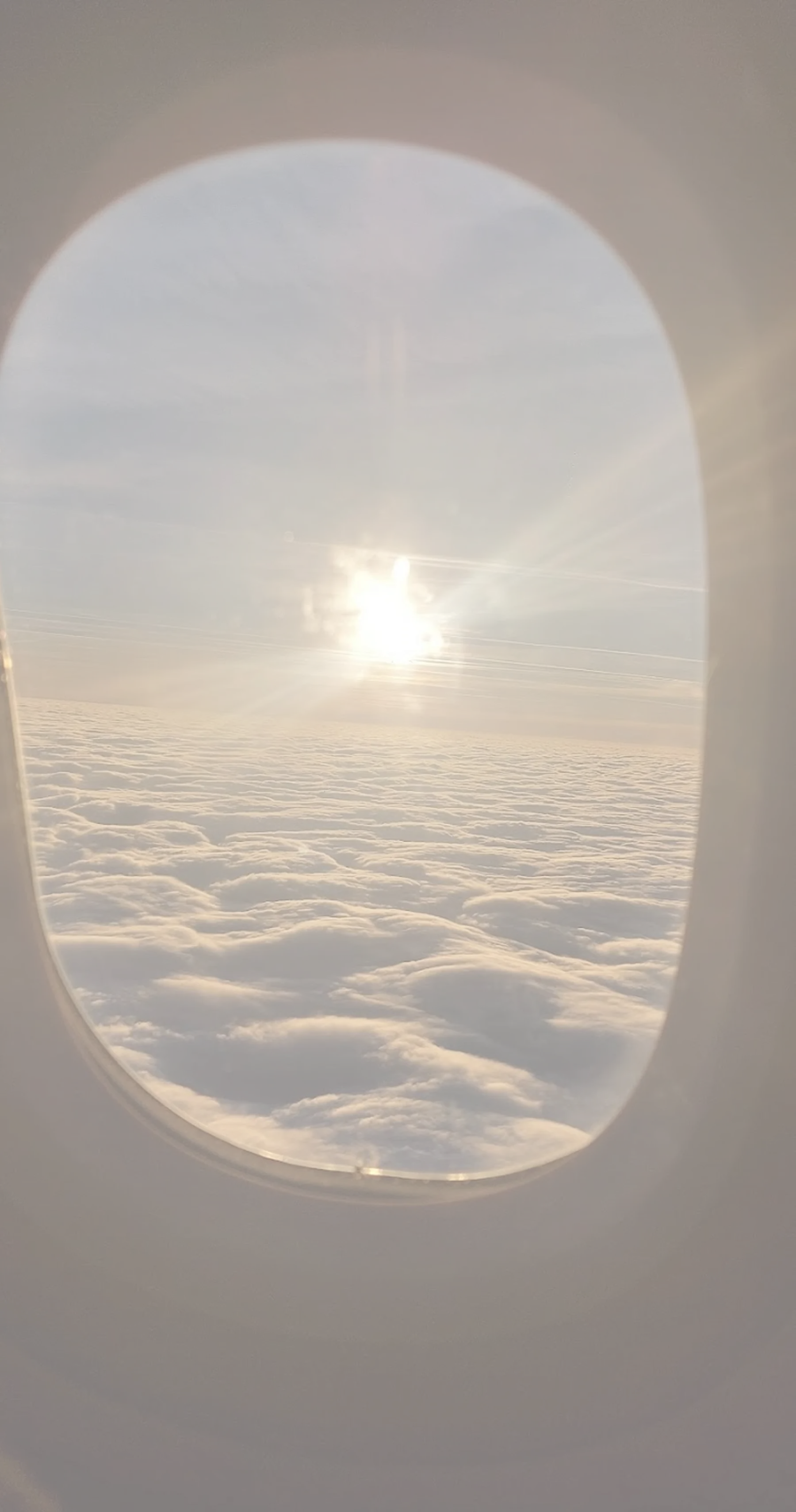 View through an airplane window of the sun setting over a thick blanket of clouds