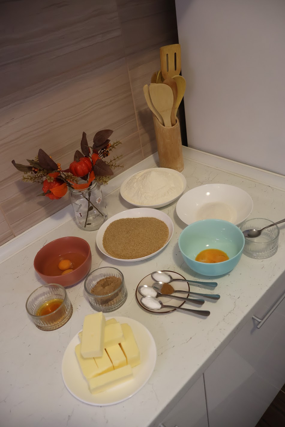 Ingredients for pumpkin spice cookies laid out on a kitchen counter: butter, brown sugar, flour, eggs, egg yolks, vanilla, pumpkin spice and measuring spoons