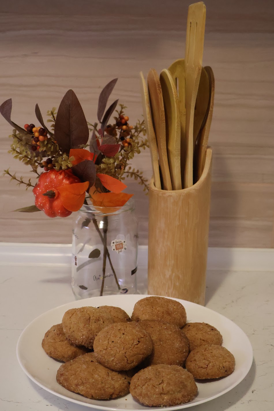 A plate of pumpkin spice cookies on the kitchen counter, next to an autumn bouquet and wooden spoons