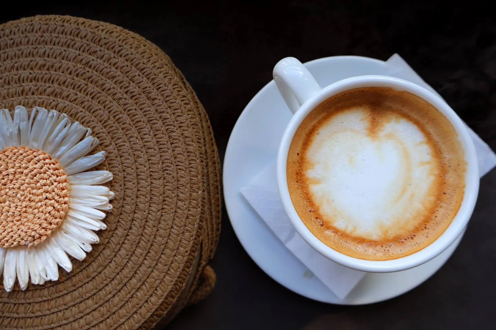 Cappuccino with a heart in the foam, next to a woven straw bag with a daisy