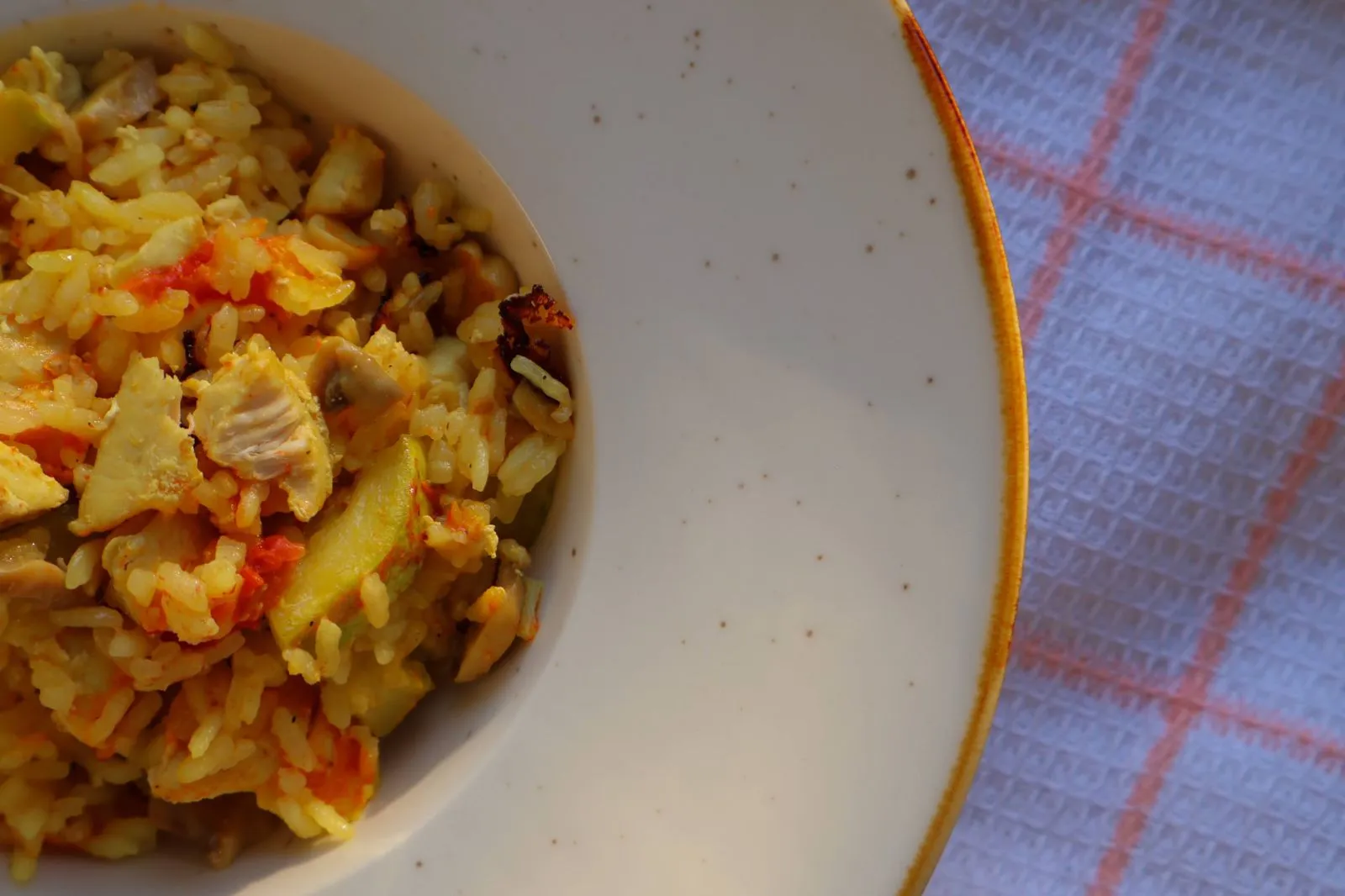 Rice with chicken and vegetables in a speckled white bowl, on a checked tablecloth