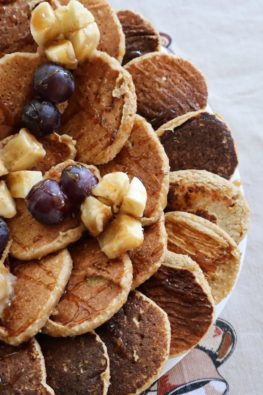 Plate of small pancakes topped with banana and grapes