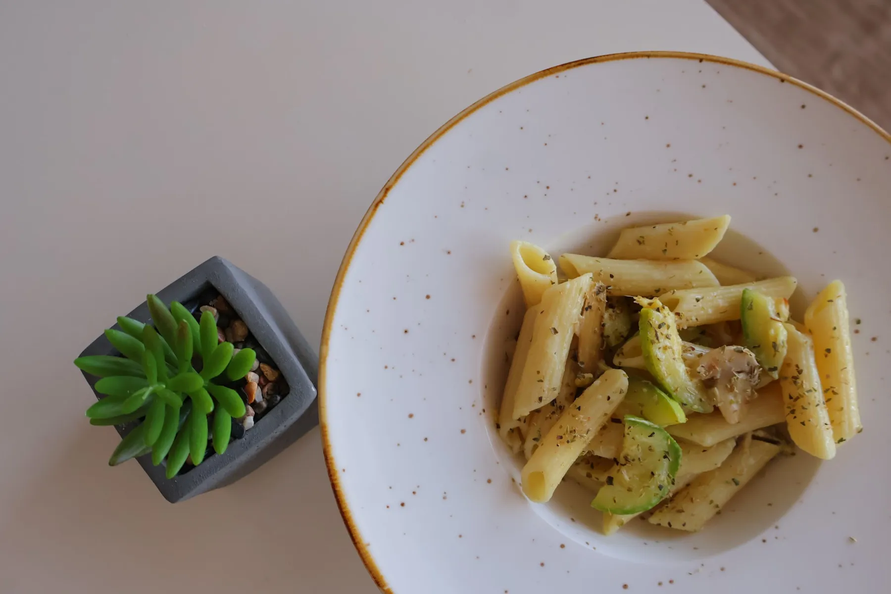 Penne with courgette in a speckled plate, next to a small succulent